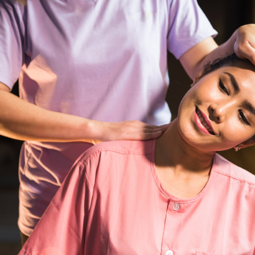 A woman with her eyes closed receiving a professional neck and shoulder massage, appearing relaxed and peaceful.