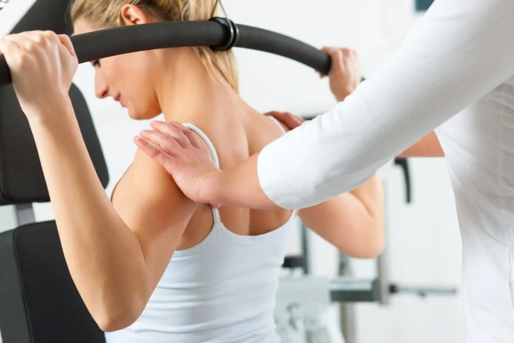 Physical therapist assisting a woman with a seated overhead back stretch.